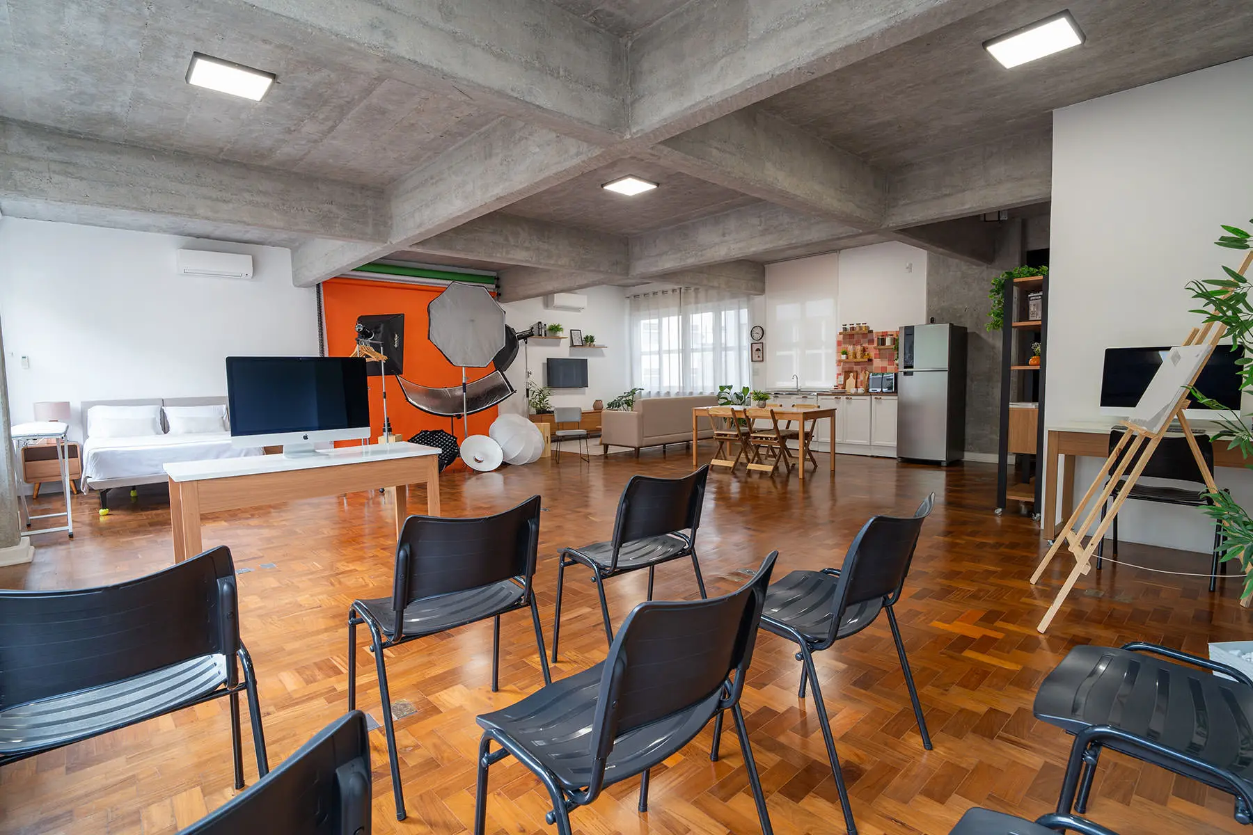 Vista ampla do estúdio: fundo infinito laranja com iluminação montada, cama, cozinha e cadeiras dispostas para turma